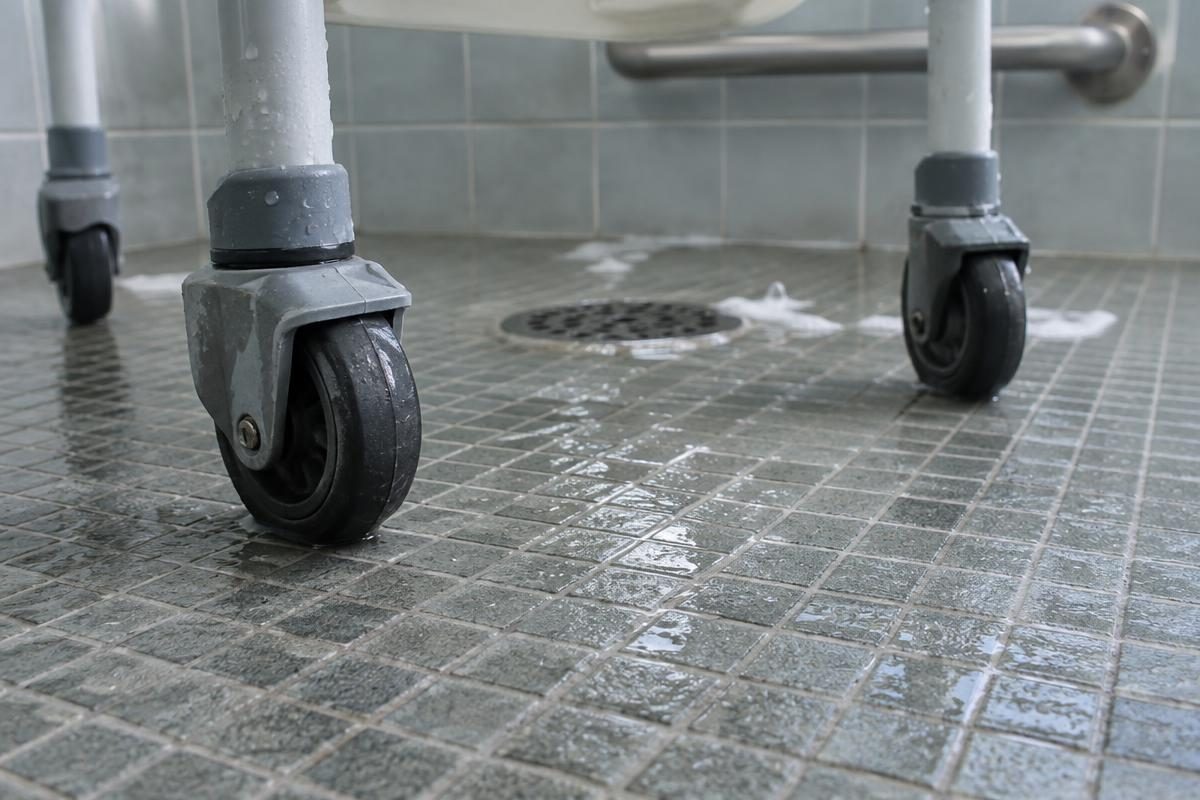 Shower chair wheels on a wet non-slip mosaic tile shower floor near the drain